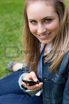 Young blonde girl sitting on the grass while sending a text
