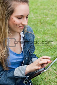 Young peaceful woman using her tablet pc while sitting on the gr