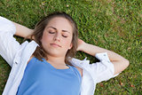 Young relaxed girl napping on the grass while placing her hands 
