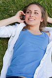 Young smiling girl lying on her back on the grass while calling 