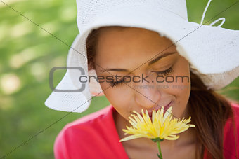 Woman wearing a white hat while smelling a flower with her eyes 