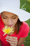 Woman wearing a white hat while smelling a flower while looking 