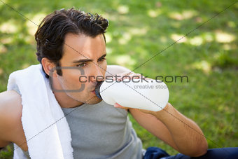 Man with a towel on his shoulder drinking from a sports bottle
