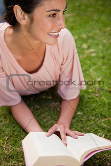 Woman looks to the side while reading a book as she is lying dow