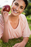 Woman holding an apple while lying in grass