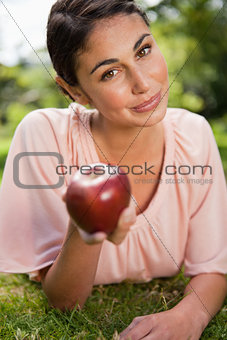 Woman offers an apple while lying in grass
