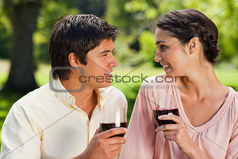 Two friends smiling towards each other while holding glasses of 
