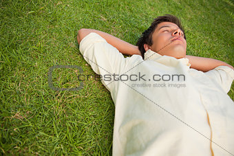 Man lying in grass with his eyes closed and his head resting on 