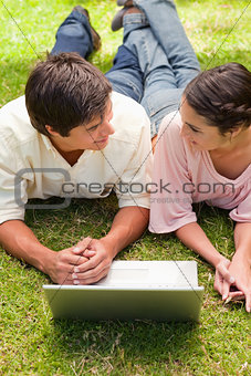 Two friends looking at each other as they lie down with a laptop
