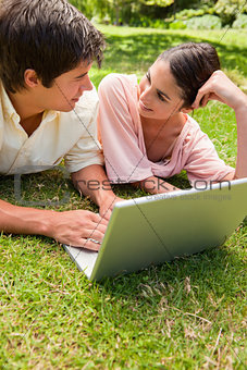 Two friends looking at each other as they use a laptop together