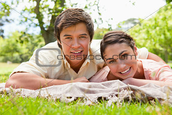 Two friends smiling while lying on their front on top of a grey 