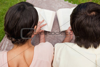 Rear view of two friends reading while on a blanket