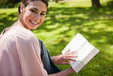 Woman looks to her side while reading a book in the grass