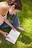 Woman looks down at a book while sitting on grass