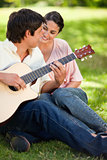 Woman smiling while watching her friend play the guitar