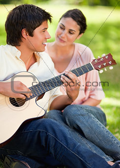 Man smiling while playing the guitar while he is being watched b