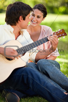 Woman smiling while her friend plays the guitar