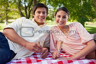 Two friends lie down on a blanket while holding champagne 