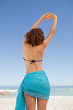 Rear view of a beautiful woman in beachwear raising her arms wit