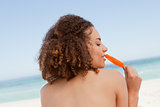 Attractive young brunette eating an orange ice lolly in front of