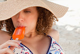 Relaxed young woman wearing a straw hat while eating an ice loll