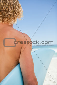 Rear view of a young blonde man holding his blue surfboard