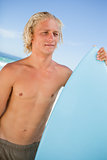 Young attractive man holding his perched surfboard in front of t