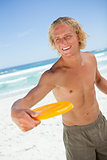Smiling blonde man standing up while playing with a yellow frisb