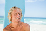 Smiling young man sitting on the beach with his surfboard