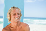 Smiling young man sitting in front of the ocean with his surfboa