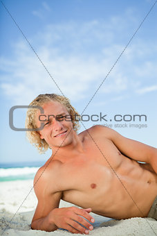 Young smiling man lying on the beach while looking at the camera