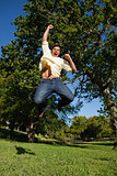 Man looking down to the ground as he jumps with his arms raised 