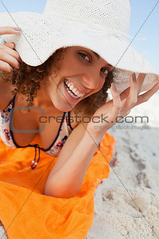 Young smiling woman holding her hat brim while lying down