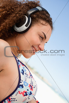 Beautiful young woman in bikini listening to music on the beach