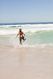 Young blonde man running in the water with his surfboard