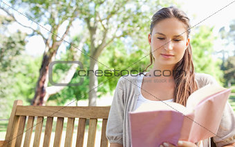 Woman sitting on a park bench while reading a book