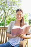 Smiling woman reading her book on a park bench