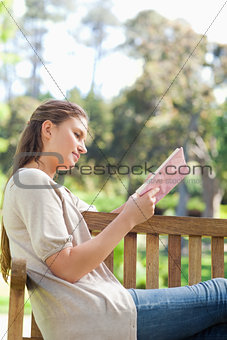 Side view of a woman reading a book on a park bench