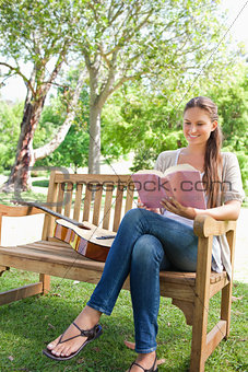 Smiling woman sitting on a bench with a book and a guitar
