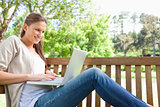 Side view of a smiling woman on a bench with her laptop