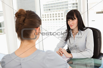 A smiling business woman listens to what the other woman has to 