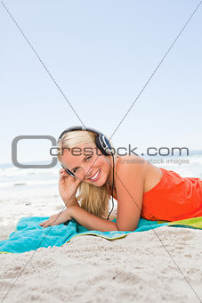 Young smiling woman lying on her beach towel while listening to 