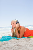 Thoughtful young woman lying on the beach while listening to mus