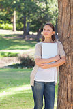 Woman with a laptop leaning against a tree