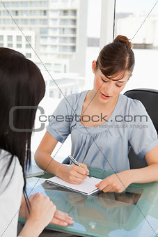 As her co-worker chats the brunette employee writes on her note 
