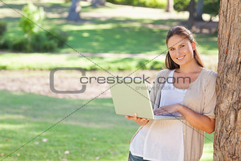 Smiling woman with a notebook leaning against a tree