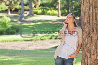 Cheerful woman on the phone leaning against a tree
