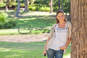 Woman with a cellphone leaning against a tree