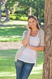 Smiling woman on her cellphone leaning against a tree