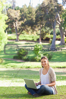 Smiling woman sitting on the lawn with her laptop